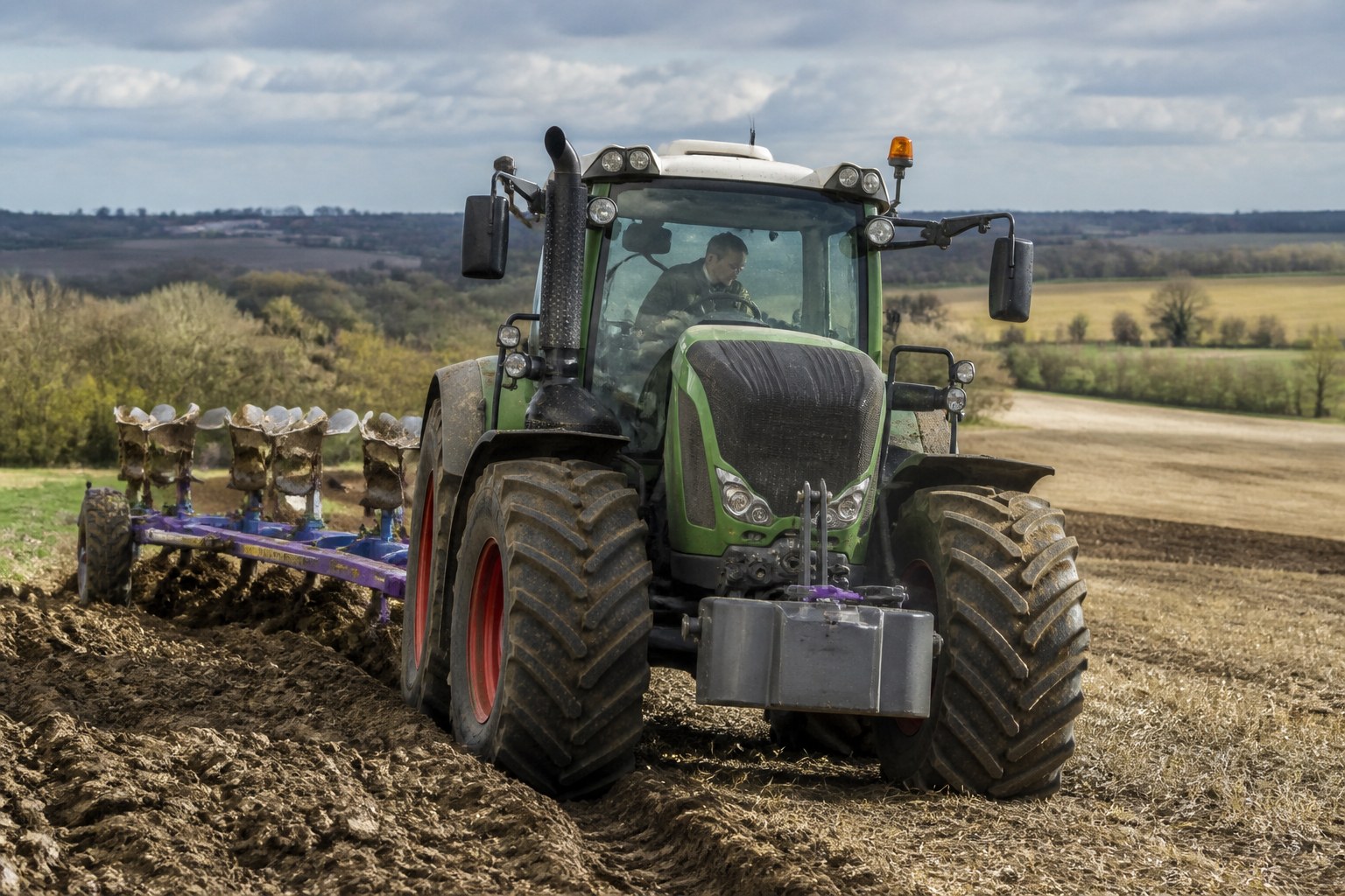 Experienced tractor driver working across an open agricultural landscape in Germany