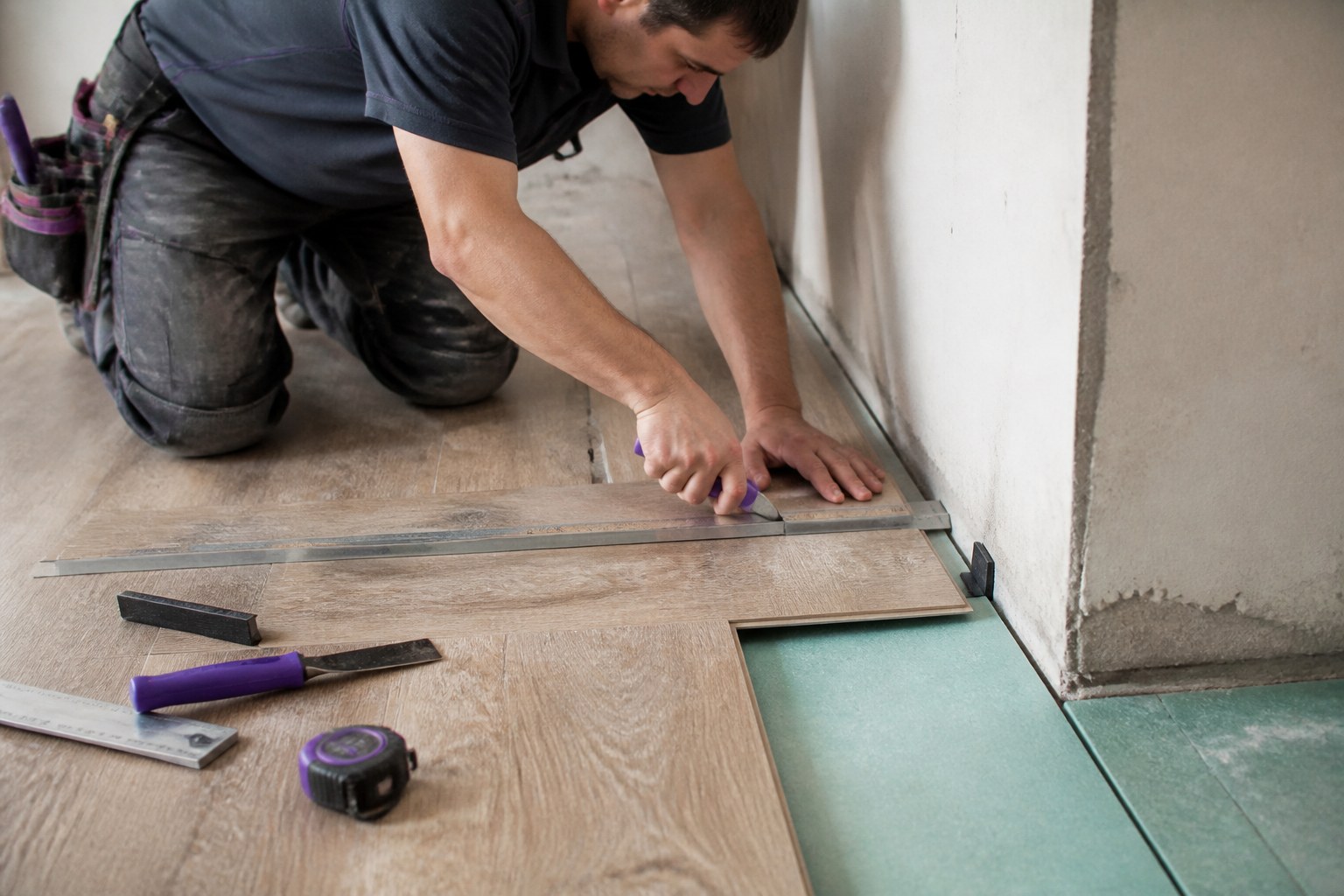 Floor layer aligning and cutting flooring material beside a prepared subfloor